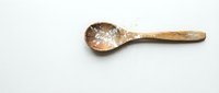 Rustic wooden spoon filled with coarse sea salt crystals on white background, natural kitchen utensil for cooking and food preparation.