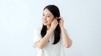 Young Asian woman with long black hair wearing white t-shirt, smiling while adjusting her hair with both hands against neutral background. Suitable for beauty, lifestyle, and wellness content.