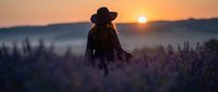 Silhouetted woman wearing cowboy hat standing in lavender field at golden sunrise with misty mountains in background.