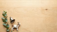 Flat lay composition with silver bell, white goat figurine, and eucalyptus branch on natural wood surface for holiday, festive, and farm-themed design projects.
