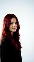 Professional woman with long burgundy red hair in black blazer looking confident on white background for business portrait photography.