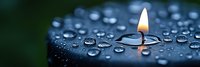 Single burning candle flame reflecting in water drops on dark surface, creating peaceful zen atmosphere against blurred green background. Panoramic meditation scene.