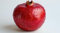 Fresh red pomegranate with water droplets isolated on white background, ready for food and beverage design projects.