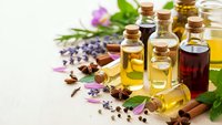 Essential oils in glass bottles with cork stoppers, lavender flowers, herbs and spices for aromatherapy, natural wellness and spa treatments on white background.