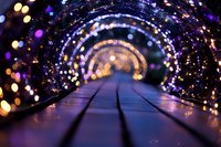 Magical illuminated tunnel with glowing bokeh lights creating spiral pattern along wooden pathway, purple and golden lights blur into dreamy perspective.