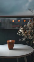 Hot chocolate with whipped cream in clay cup on round table, moody atmospheric setting with dried flowers and bokeh lights creating cozy autumn ambiance.