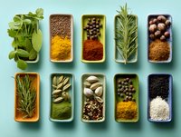 Aromatic herbs and colorful spices in small ceramic containers arranged in neat rows on turquoise background for cooking and food styling.