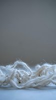 Natural white cotton fibers and threads in soft tangled pile against neutral gray background for textile industry and organic material concepts.