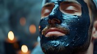 Close up of young caucasian man with black clay mask during spa treatment. Luxury skincare and wellness concept with warm ambient lighting and bokeh effect in background.