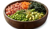 Fresh poke bowl with raw tuna, avocado, edamame, carrots and seaweed in wooden bowl, healthy asian cuisine preparation on white background.