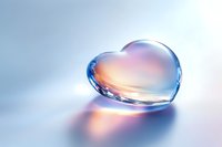 Crystal clear heart shape on soft blue background with gentle orange and pink reflections creates romantic mood for valentines day designs and love concepts.