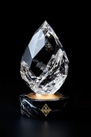 Crystal teardrop shape on luxurious black marble and gold pedestal against dark background, featuring geometric design detail and dramatic lighting effects.