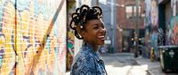 Young African American woman with natural curly hair laughing joyfully in colorful urban street with graffiti art background for lifestyle and happiness concepts.