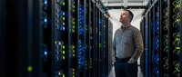 Professional IT technician examining server infrastructure in modern data center with glowing network equipment and advanced computing technology.