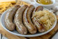 Grilled bratwurst sausages served on white plate with sauerkraut and mustard sauce, traditional German cuisine close up view on rustic wooden board.