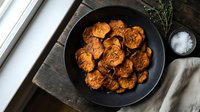 Golden brown sweet potato rounds cooked in cast iron skillet with fresh herbs and sea salt on rustic wooden cutting board for healthy cooking recipes.