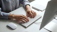 Professional businesswoman typing on laptop computer at modern office desk with documents and mouse nearby for corporate work productivity.