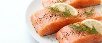 Fresh raw salmon fillets with dill herbs and lemon slices on white plate, seasoned with black pepper for healthy cooking and gourmet seafood preparation.