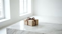 Kraft paper gift box with brown ribbon bow on marble surface in bright minimalist white room, elegant holiday present concept.