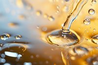 Macro photography of golden liquid drops and splashes with reflective surface creating abstract pattern in warm amber tones against blurred background.