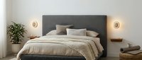 Modern minimalist bedroom with gray upholstered headboard, neutral bedding, warm lighting and houseplant for contemporary interior design projects.