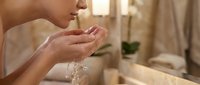 Young woman with medium skin tone rinsing hands under running water in modern bathroom, demonstrating daily hygiene routine and personal care practices.
