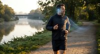 Young athletic Caucasian man jogging along scenic river path during golden hour sunrise workout session for healthy lifestyle and fitness motivation.
