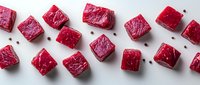 Raw beef cubes cut into uniform pieces scattered on white background, fresh red meat chunks with black peppercorns, ready for cooking preparation.