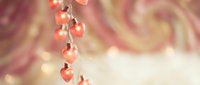 Romantic pink heart-shaped decorations hanging on string against soft blurred background with warm golden bokeh lights for Valentine's Day celebrations.