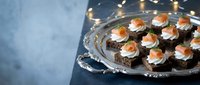 Elegant appetizers with smoked salmon and cream cheese on dark bread served on silver tray with festive lighting for holiday entertaining and special occasions.