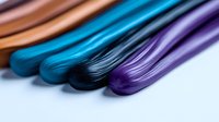 Colorful hair extensions in vibrant blue, purple, brown and black shades arranged in rows on white background, showing texture and shine of synthetic fibers.