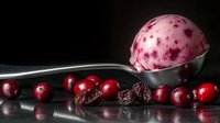 Scoop of berry ice cream with fresh and dried cranberries on dark reflective surface, dramatic food photography with selective lighting and black background.