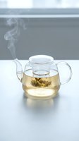 Glass teapot with steaming herbal tea and infuser basket, perfect for beverage, wellness, and kitchen lifestyle content.