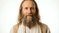 Middle-aged Caucasian man with long brown hair and full beard wearing white robes against neutral background for spiritual or historical concepts.