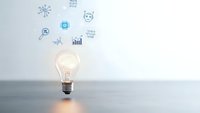 Glowing light bulb with floating digital innovation icons representing creative business ideas, technology solutions and strategic planning concepts.