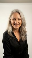 Confident mature Caucasian businesswoman with silver gray hair smiling warmly in black blazer against neutral background for professional headshot.