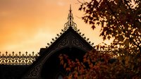 Ornate Victorian house roofline with decorative gingerbread trim silhouetted against golden sunset sky creating atmospheric architectural scene.