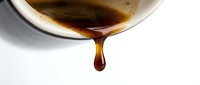Pouring dark liquid syrup or caramel from a white bowl against white background, isolated for culinary and food design projects.