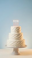 Three-tier white birthday cake with lit candles on pedestal stand against soft blue background for celebration and party design.
