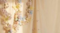 Delicate Easter egg garland with pastel colors and spring blossoms hanging on warm beige wall creating festive seasonal home decoration atmosphere.