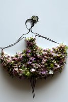 Creative floral art showing feminine silhouette in dress made of fresh purple and white flowers with elegant hair bun, arranged on light background.