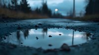Moody reflection of full moon in roadside puddle during blue hour, with silhouettes of pine trees against dramatic evening sky. Atmospheric nature photography.