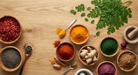 Colorful assortment of superfoods and spices in wooden bowls on rustic table, top view, featuring turmeric, ginger, chia seeds, and goji berries.