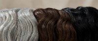 Hair extensions in different colors from silver gray to black arranged in wavy bundles on neutral background for beauty salon services.