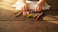 Child hands selecting colorful crayons on wooden table with drawing papers, creative art activity for kids education and artistic development at home.