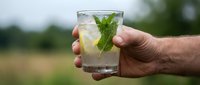 Refreshing mojito cocktail with fresh mint leaves and ice held in male hand outdoors against blurred natural background, perfect for beverage and summer drink concepts.