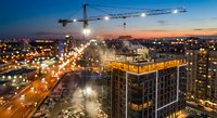 Construction site with tower crane building modern structure at sunset with city lights and urban development progress in metropolitan area.