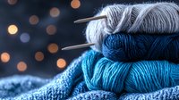 Cozy knitting composition with blue and gray yarn balls, metal needles on blurred bokeh background, warm winter crafting atmosphere for hobby projects.