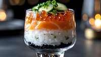 Fresh salmon sashimi layered with sushi rice and black caviar in glass, topped with red roe, cucumber slices and microgreens against dark background with bokeh.