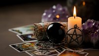 Mystical fortune telling setup with tarot cards, crystal ball, pentagram pendant, burning candle and amethyst crystals for spiritual guidance and divination.